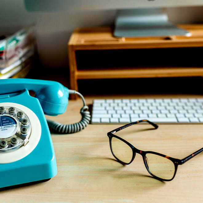 A bright blue phone on a desk next to a pair of glasses